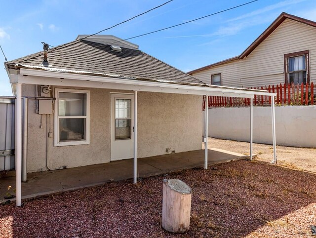 exterior space featuring roof with shingles, fence, and stucco siding