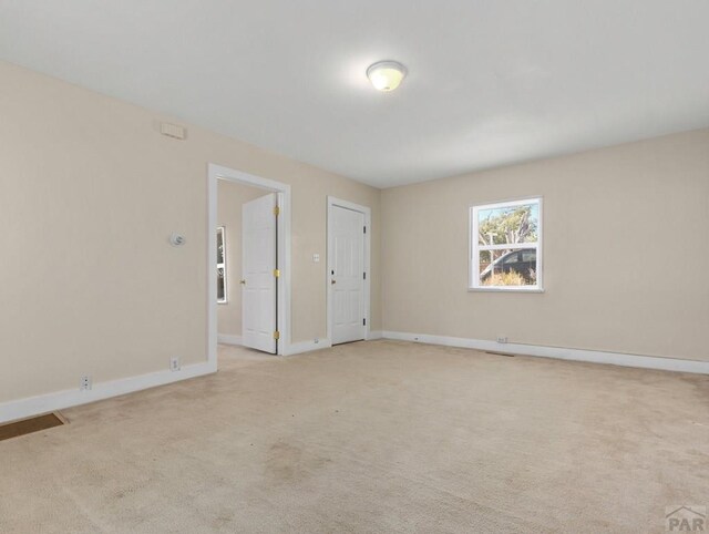 spare room with baseboards and light colored carpet