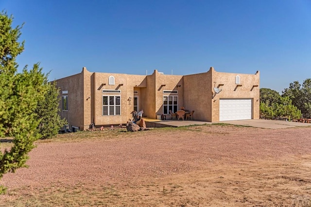 pueblo-style house featuring driveway, a garage, and stucco siding