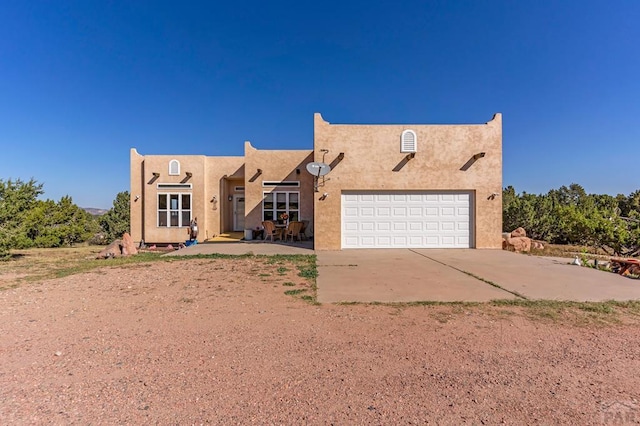 pueblo-style home with concrete driveway, an attached garage, and stucco siding