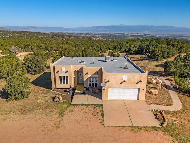 view of front of property featuring stucco siding, a mountain view, a view of trees, a garage, and driveway