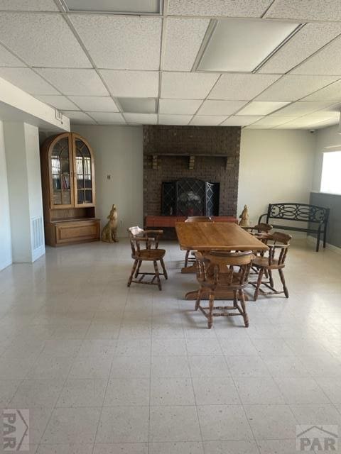 dining room featuring a paneled ceiling, a fireplace, baseboards, and tile patterned floors