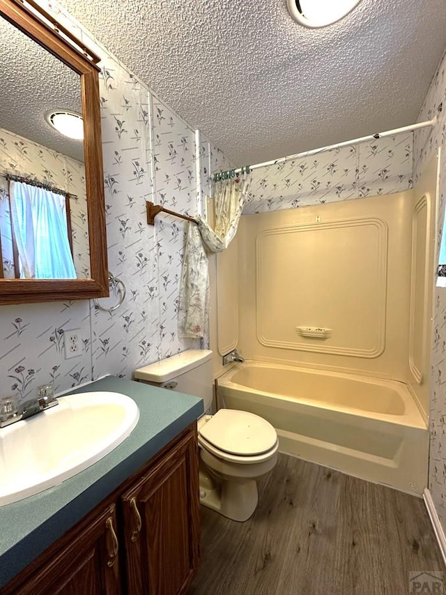 full bathroom with a textured ceiling, toilet, wood finished floors, vanity, and wallpapered walls