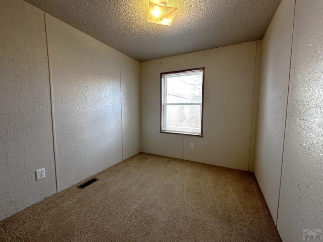 carpeted spare room featuring a textured ceiling, a textured wall, and visible vents