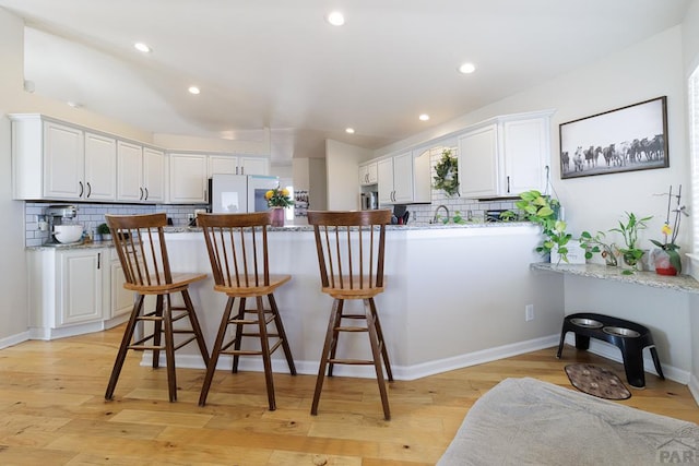 kitchen with light wood-type flooring, freestanding refrigerator, a peninsula, and a breakfast bar area