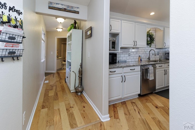 kitchen with tasteful backsplash, dishwasher, light wood-type flooring, white cabinetry, and a sink