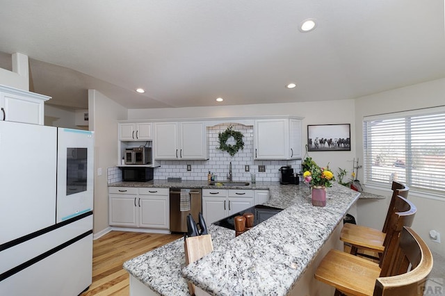 kitchen featuring dishwashing machine, white cabinetry, a sink, and freestanding refrigerator