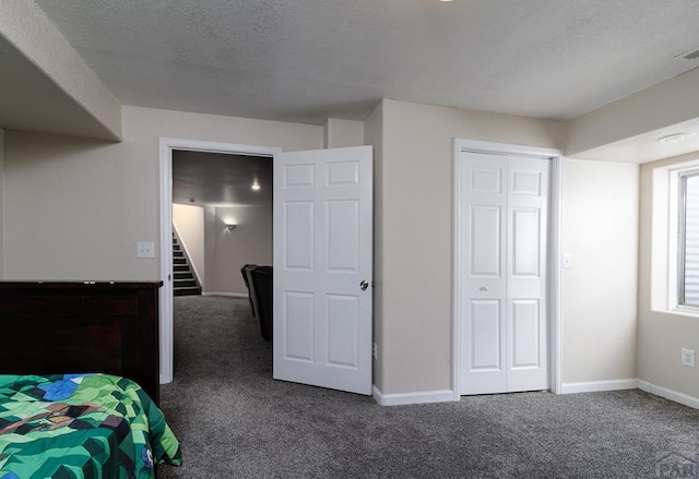 unfurnished bedroom featuring dark colored carpet, a closet, a textured ceiling, and baseboards