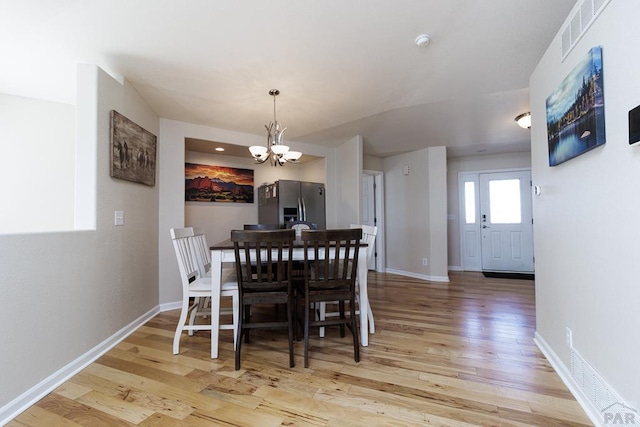 dining area featuring visible vents, light wood-style flooring, baseboards, and an inviting chandelier