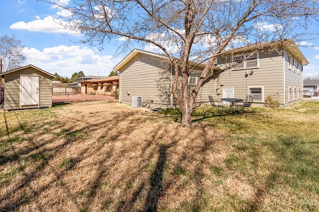 back of house featuring fence, central air condition unit, an outdoor structure, a lawn, and a storage unit