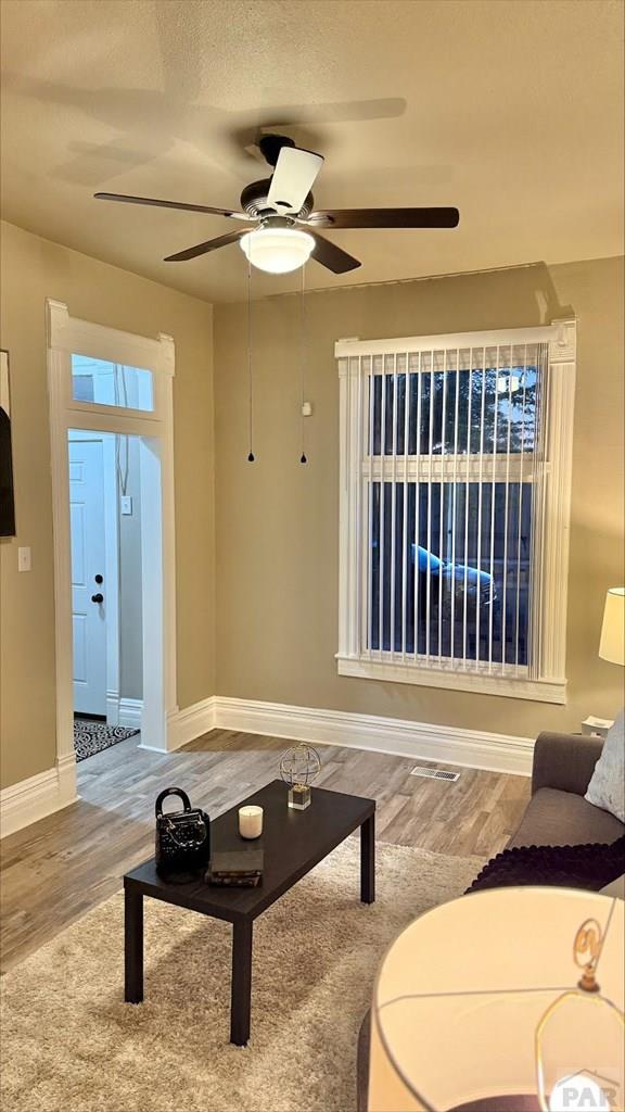 living area with baseboards, ceiling fan, wood finished floors, and visible vents