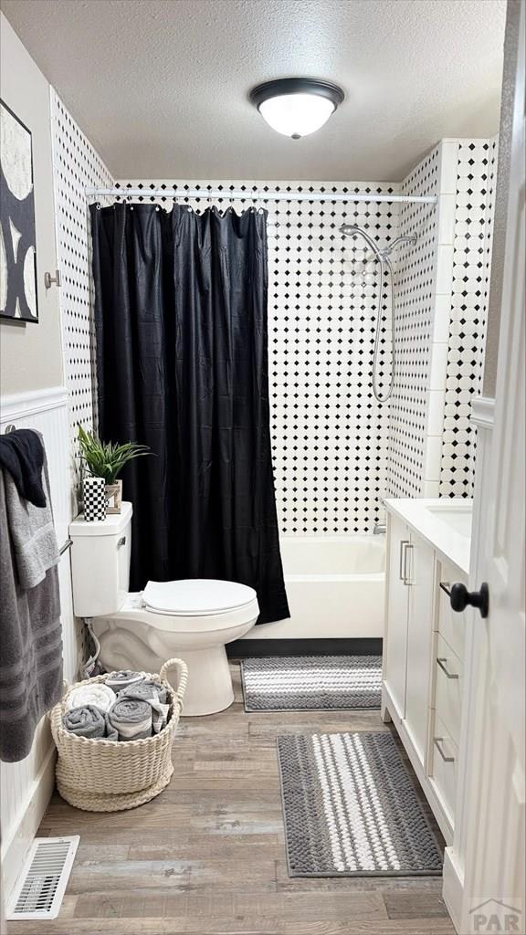 full bathroom featuring wood finished floors, toilet, a textured ceiling, and visible vents