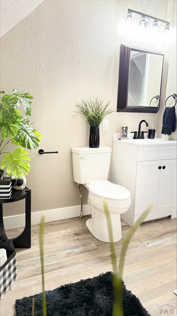 half bathroom featuring vanity, a textured wall, wood finished floors, toilet, and baseboards