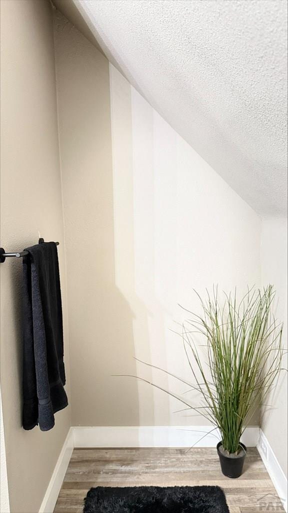 bathroom featuring baseboards, a textured ceiling, wood finished floors, and vaulted ceiling