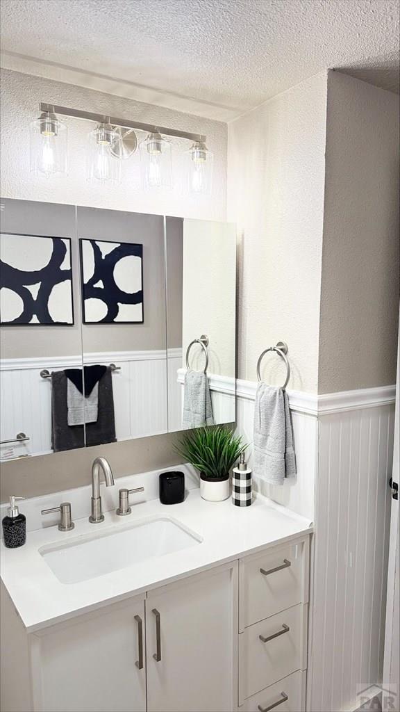 bathroom featuring a textured wall, a decorative wall, vanity, a textured ceiling, and a wainscoted wall