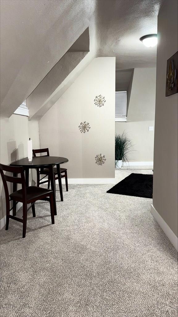 dining room featuring vaulted ceiling, baseboards, carpet flooring, and a textured ceiling