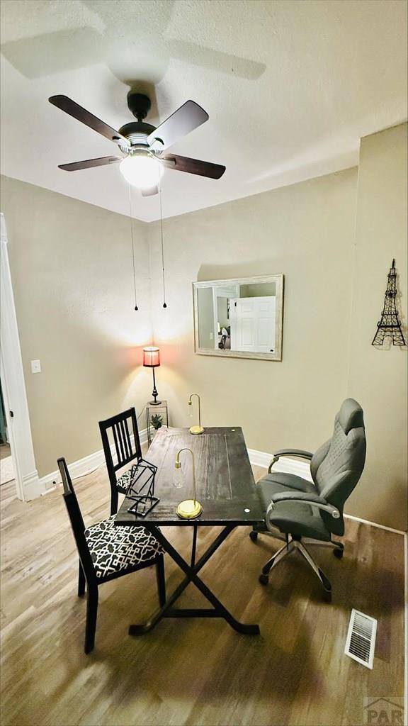 interior space with baseboards, a ceiling fan, wood finished floors, and visible vents