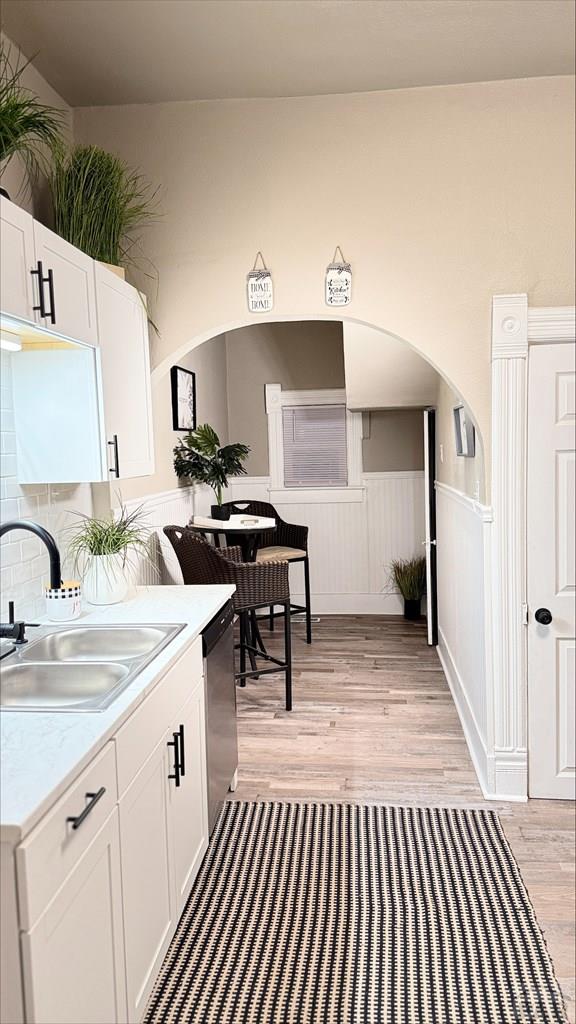 kitchen with stainless steel dishwasher, light wood-style floors, light countertops, white cabinetry, and a sink