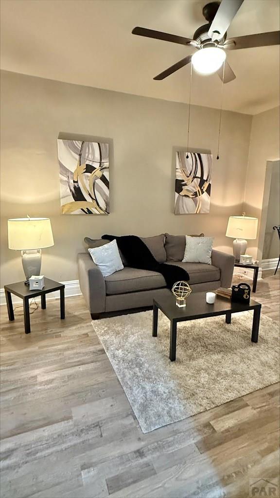 living room with baseboards, ceiling fan, and wood finished floors
