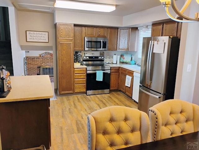 kitchen with light wood finished floors, stainless steel appliances, light countertops, brown cabinetry, and a sink