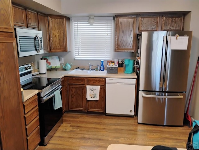 kitchen with light wood-style flooring, stainless steel appliances, a sink, and light countertops