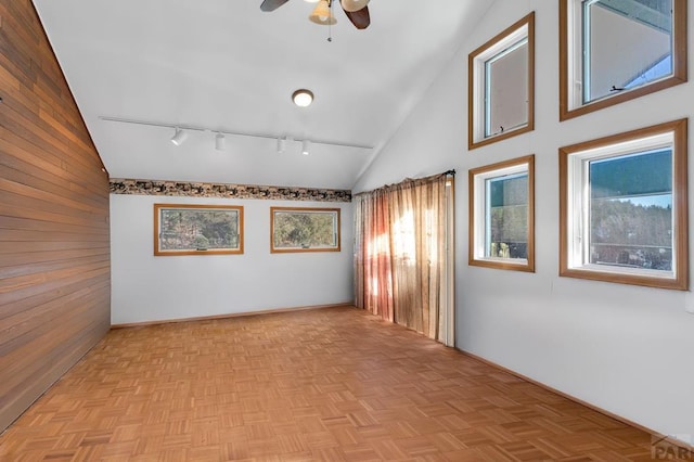 unfurnished room featuring high vaulted ceiling, wood walls, track lighting, and a ceiling fan