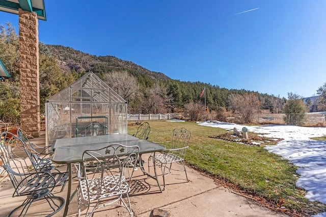 view of patio featuring an outbuilding, a greenhouse, outdoor dining space, a mountain view, and fence