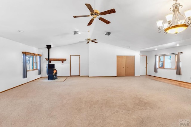 unfurnished living room featuring a wood stove, light carpet, visible vents, and lofted ceiling