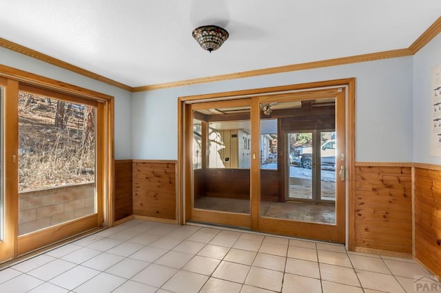 doorway with wood walls, light tile patterned flooring, crown molding, and wainscoting