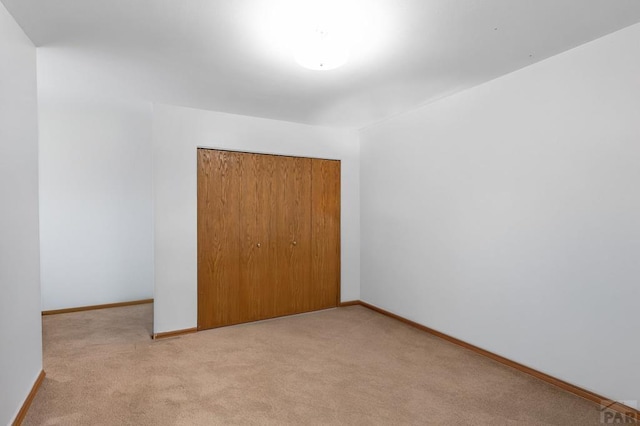 unfurnished bedroom featuring light carpet, baseboards, and a closet