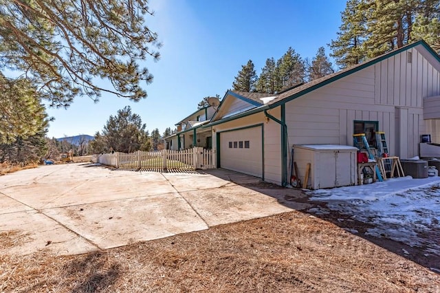 view of side of home featuring a garage, concrete driveway, a mountain view, and fence