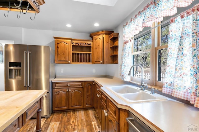 kitchen with appliances with stainless steel finishes, brown cabinets, light wood-style floors, open shelves, and a sink