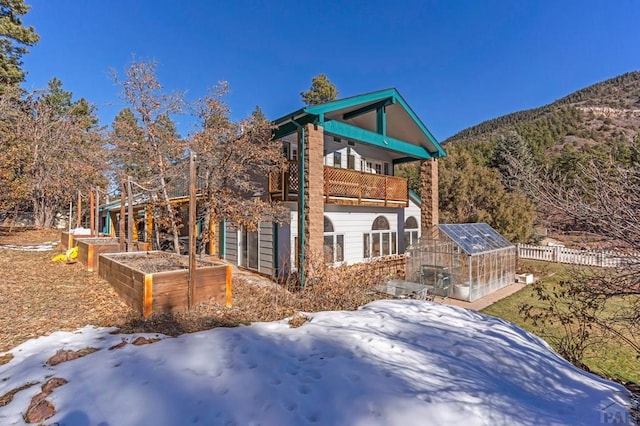 view of snowy exterior with an outbuilding, a mountain view, fence, a garden, and an exterior structure