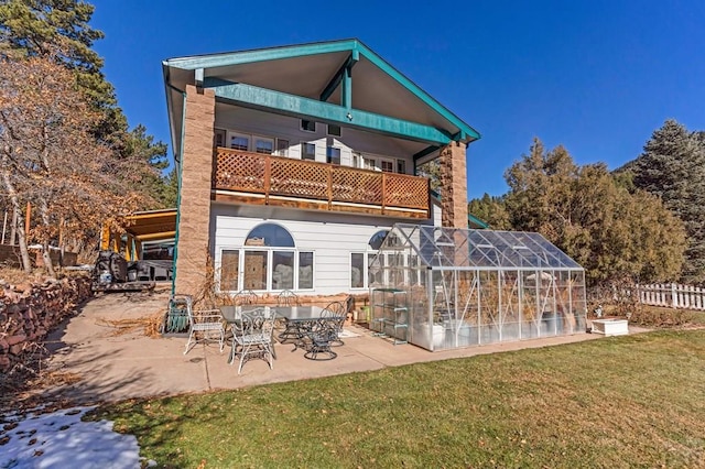 back of property with a lawn, an outdoor structure, a greenhouse, and a balcony