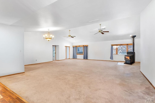 unfurnished living room featuring light carpet, vaulted ceiling, ceiling fan with notable chandelier, and a wood stove