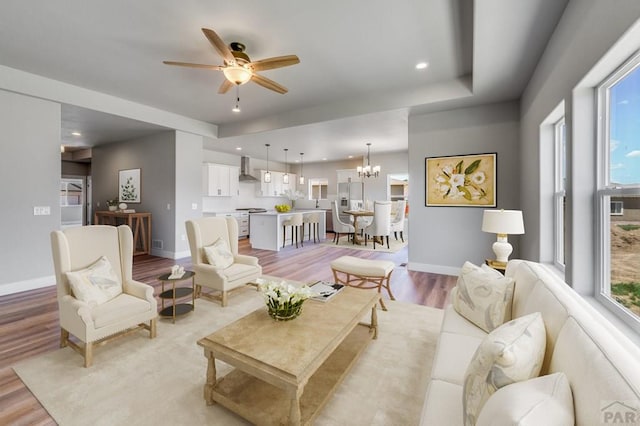 living area featuring light wood-style floors, ceiling fan with notable chandelier, baseboards, and recessed lighting