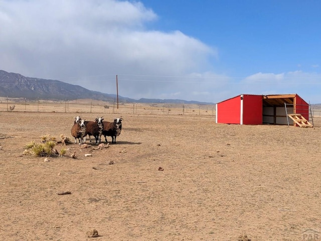 view of yard featuring fence, a pole building, an outdoor structure, a rural view, and a mountain view