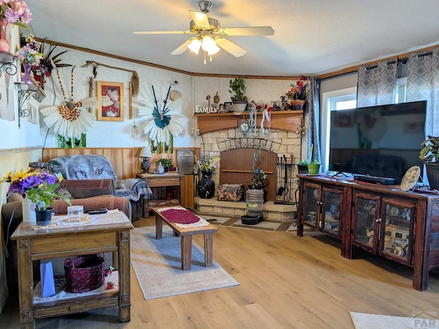 living room featuring ornamental molding, a fireplace, wood finished floors, a textured ceiling, and a ceiling fan