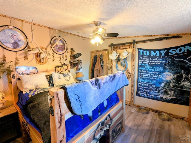 miscellaneous room featuring a barn door, a textured ceiling, wood finished floors, and a ceiling fan