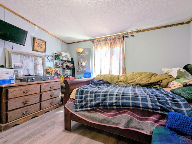 bedroom with a textured ceiling, wood finished floors, and ornamental molding