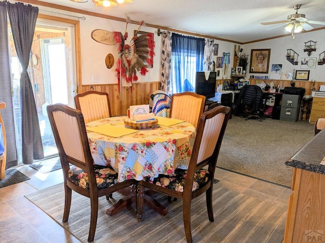 dining area featuring wooden walls, crown molding, carpet, wainscoting, and a ceiling fan