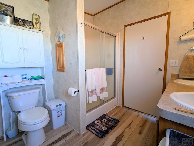 bathroom featuring wood finished floors, a stall shower, ornamental molding, a sink, and toilet