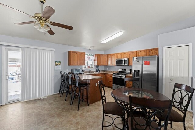 kitchen featuring a ceiling fan, appliances with stainless steel finishes, a breakfast bar area, vaulted ceiling, and a sink