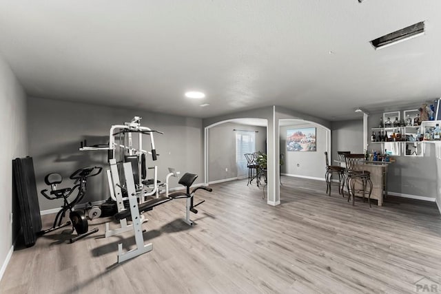 workout area featuring arched walkways, baseboards, a dry bar, and wood finished floors