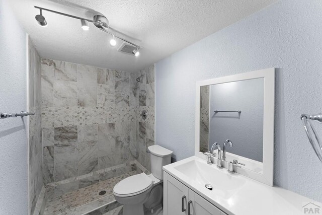 full bath featuring visible vents, toilet, a textured ceiling, vanity, and tiled shower