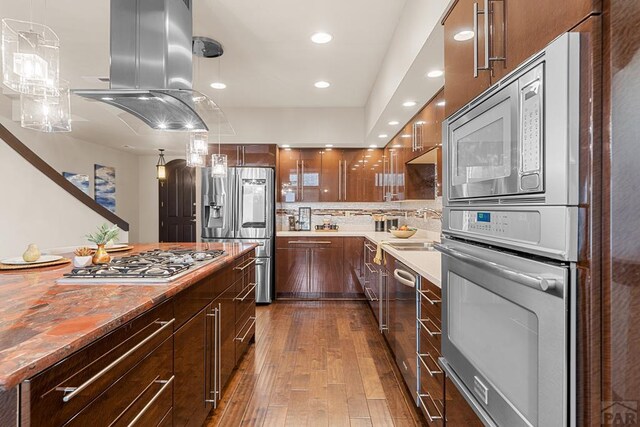 kitchen featuring stainless steel appliances, light countertops, hanging light fixtures, dark wood-type flooring, and island range hood