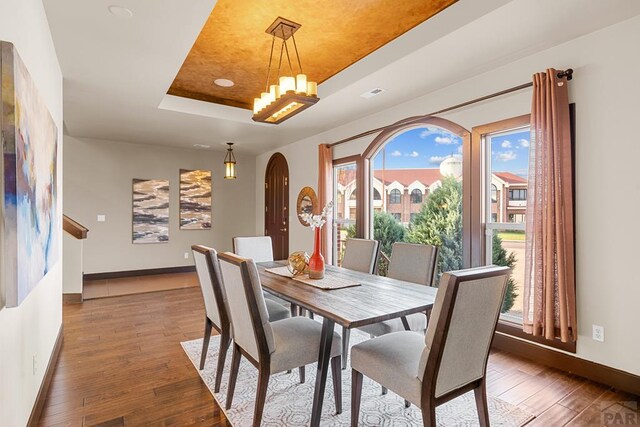 dining room featuring a tray ceiling, dark wood finished floors, arched walkways, and an inviting chandelier