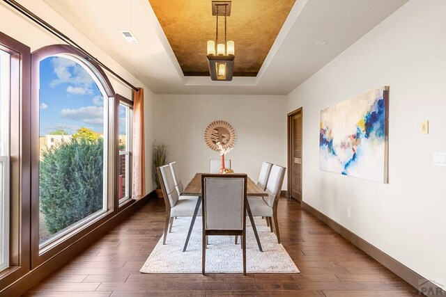 dining area featuring dark wood-type flooring, a raised ceiling, visible vents, and baseboards