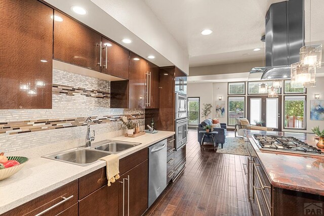 kitchen with stainless steel appliances, a sink, hanging light fixtures, tasteful backsplash, and island exhaust hood