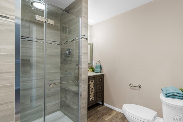 bathroom with toilet, wood finished floors, vanity, baseboards, and a stall shower